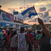 Des migrants marchent au soleil couchant, un drapeau guatémaltèque flotte dans les airs.