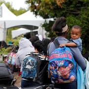 Un enfant dans les bras d'une femme dans une file d'attente devant un chapiteau