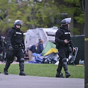 Des policiers antiémeute marchent en rang devant des tentes démontées.