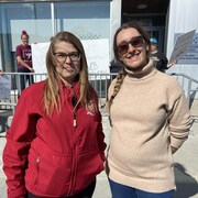 Andréane Brouard et Alisée Lemire Lemay posent pour la caméra devant des manifestantes face aux bureaux de la députée.