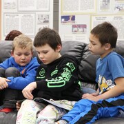 Une femme supervise la lecture d'un groupe de trois enfants assis sur un canapé en cuir.