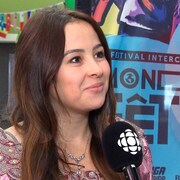 Une femme de profil, qui sourit, avec un micro décoré du logo de Radio-Canada pointé vers elle.