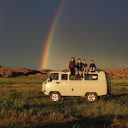 Un arc-en-ciel traverse le ciel. Les enfants sont juchés sur le toit de leur caravane.