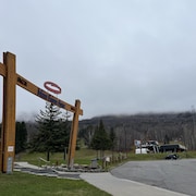 Une arche de bois où l'on peut lire «Mont-Sainte-Anne», et «RCR». La montagne se trouve en arrière-plan.