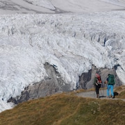 Deux personnes marchent sur une partie gazonnée en direction d'un immense glacier. 