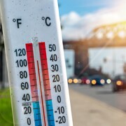Un thermomètre devant les voitures et la circulation pendant la canicule à Montréal.