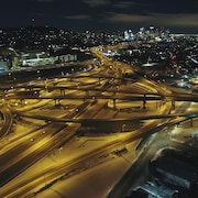 Une vue aérienne et de nuit de l'échangeur Turcot, avec au fond le centre-ville de Montréal.