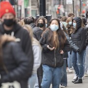 De jeunes gens font la file sur le trottoir en portant un masque.