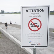Une affiche d'interdiction de baignade avec des promeneurs en arrière plan.