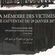 Plan rapproché du monument à la mémoire des victimes de l’attentat du 29 janvier 2017 en hiver. On peut y lire une citation de Khalil Gibran en français et en arabe qui se lit comme suit : «Nul ne peut atteindre l’aube sans passer par le chemin de la nuit».