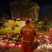 Une femme prie au pied d'un monument où sont déposées des gerbes de fleurs.