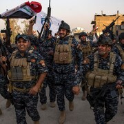 Des agents de la police fédérale irakienne manifestent leur joie en brandissant leurs armes et des drapeaux.