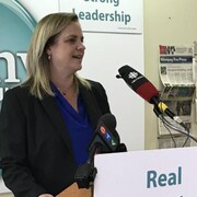 Jenny Motkaluk devant un micro dans un quartier général de campagne, et Brian Bowman à l'extérieur devant les micros des journalistes, en compagnie de son épouse Tracy.