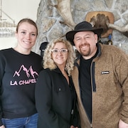 Mylène Aubry, Lina Morin et Charles Marchand, Domaine l'Or-Piste prient en photo devant un foyer en pierre. 