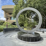 Une imposante sculpture en forme d'anneau se dresse devant un bâtiment aux lignes courbes.