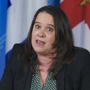 Mylène Drouin parle dans un micro devant des drapeaux du Québec et de Montréal.