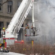 Les pompiers arrosent la façade d'un immeuble d'où s'échappe une épaisse fumée.