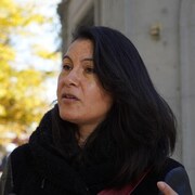 Une femme aux longs cheveux noirs en plan rapproché avec des arbres derrière elle.