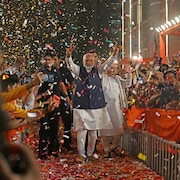 Narendra Modi marche sous une pluie de confettis, dans une allée clôturée au centre d'une foule, en montrant, les bras tendus, le signe de la victoire.