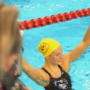 Une nageuse debout dans une piscine lève les bras en l'air en signe de satisfaction.