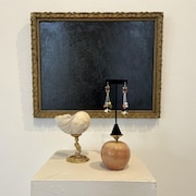 Un coquillage, des bijoux et une pomme devant un cadre. 