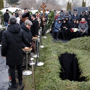 Des gens rassemblés autour d'un trou dans le sol, dans un cimetière