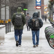 Deux hommes marchent sur un trottoir du centre-ville sous la neige.