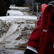 Un skieur marche sur un terrain partiellement enneigé. 