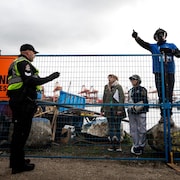 Quatre personnes, dont un policier, devant les grilles du campement du parc CRAB.