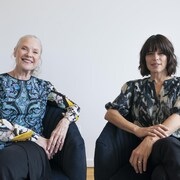 Les deux femmes sourient, assises côte à côte, sur des fauteuils. 