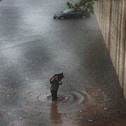 Un homme marche avec de l'eau jusqu'aux genoux. Au fond, on voit une voiture abandonnée au milieu de l'eau.
