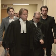 Daigle est vêtu d'un complet gris pâle alors que Siciliano porte un complet noir. Ils marchent derrière leurs avocats.