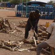 Des hommes coupent du bois près d'un vendeur de bonbonnes de gaz. 