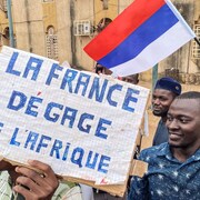 Un Nigérien tient un drapeau de la Russie et une pancarte qui porte la mention « La France dégage de l'Afrique ».