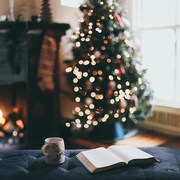 Photo montrant un livre et une tasse devant un sapin de Noël et un feu de cheminée.