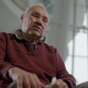 Un homme âgé est assis dans une salle avec beaucoup de fenêtres.