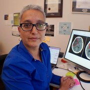 Une femme assise devant un ordinateur sur lequel on voit deux scans du cerveau.