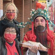 Un homme portant un costume pose en compagnie de deux femmes dans une rue.