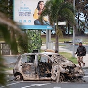 Des personnes marchent à côté d'une voiture incendiée.