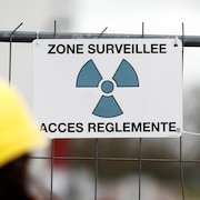Affiche avec un symbole de radioactivité. Il est écrit «Zone surveillée. Accès réglementé.»