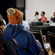 Un homme qui porte une tuque est assis et regarde des gens parler dans un micro lors d'une assemblée générale, à Iqaluit, le 16 septembre 2023.