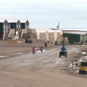 Deux enfants et un homme en quatre-roues dans une rue de Naujaat, au Nunavut, en 2016.