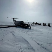 Un avion à hélices sur la neige entouré de gens et de motoneiges, le 7 mai 2024.