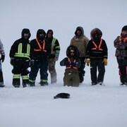 Un groupe de personne vêtu chaudement attendent dans la neige. 