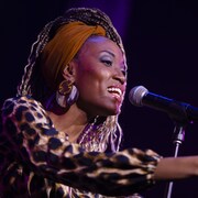L'autrice-compositrice-interprète Nyenimana sur scène chantant derrière un micro et tendant la main.