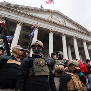 Des membres du groupes sur les marches du Capitole habillés avec des vêtements de combat et des casques.
