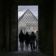 Quatre personnes devant la pyramide du musée du Louvre, à travers l'ouverture d'une porte.