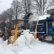 Un tracteur souffle de la neige dans la benne d’un camion lors d’une opération de déneigement.