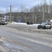 Deux voitures de police encerclent une voiture stationnée avec le coffre arrière ouvert.