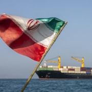 Le drapeau de l'Iran flotte avec un navire commercial en arrière plan.
